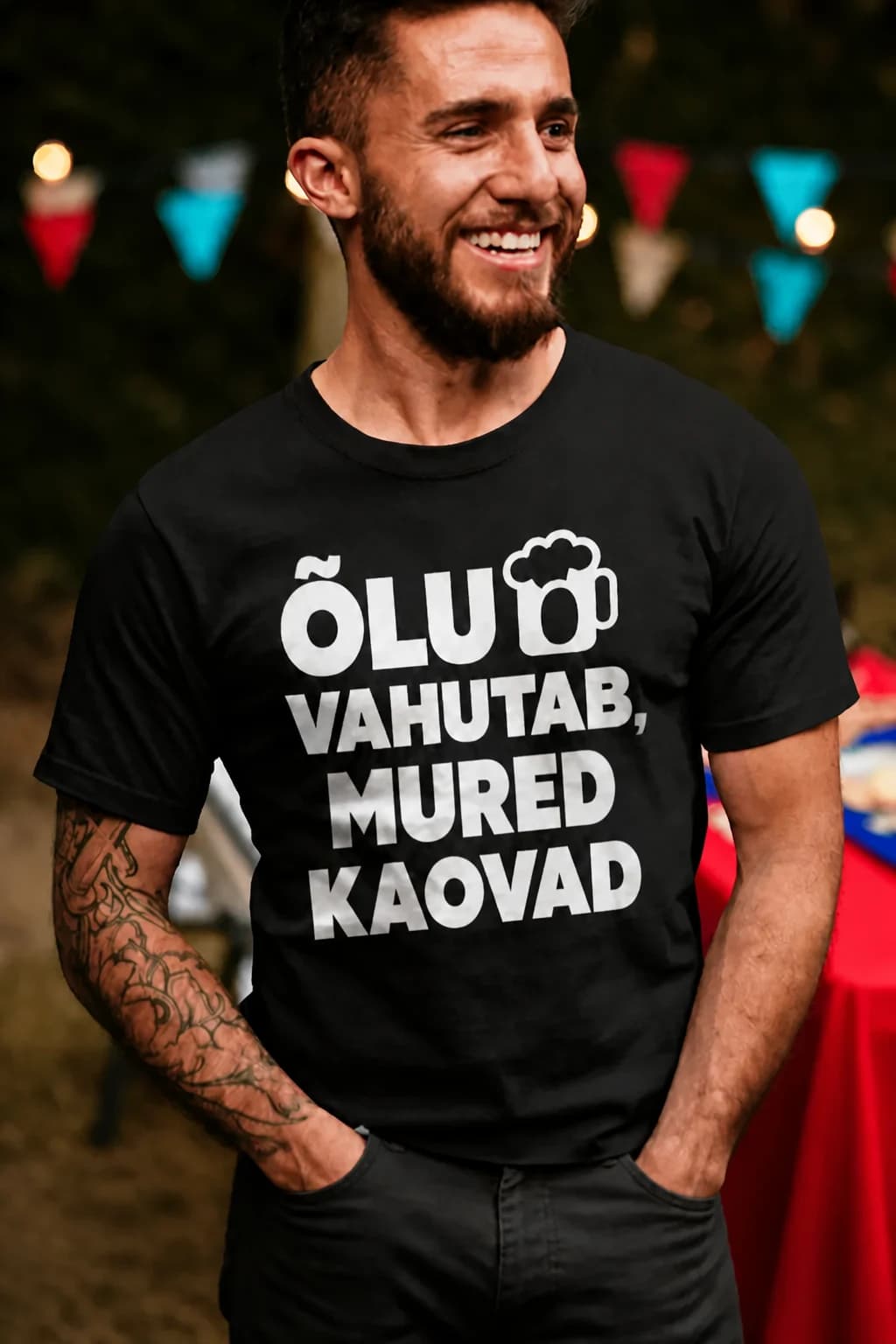 Naeratav habemega mees mustas naljakas T-särgis, vahutav õllekann ja kiri „Õlu vahutab, mured kaovad“