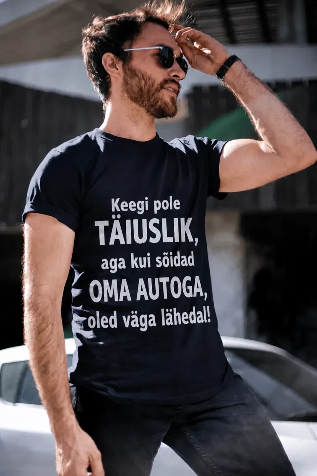 Päikeseprillidega mees mustas T-särgis kirjaga „Keegi pole täiuslik, aga … oled väga lähedal!“ – T-särk autojuhile