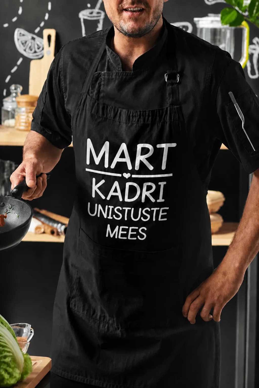Mees mustas põlles, millel valge kiri „MART“ ja „KADRI UNISTUSTE MEES“ – põll nimega kingituseks mehele